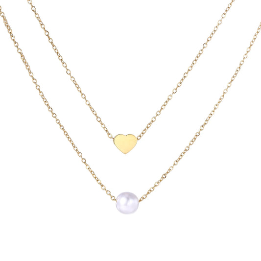 Two delicate gold-plated chains with heart charm and white pearl bead on cream background, minimal layered design.