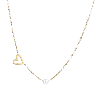 Delicate gold necklace with open heart charm and white pearl bead on fine chain against cream background